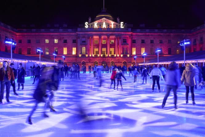 People skating at night on the Somerset House ice skating rink with dazzling light displays illuminating them on the ice