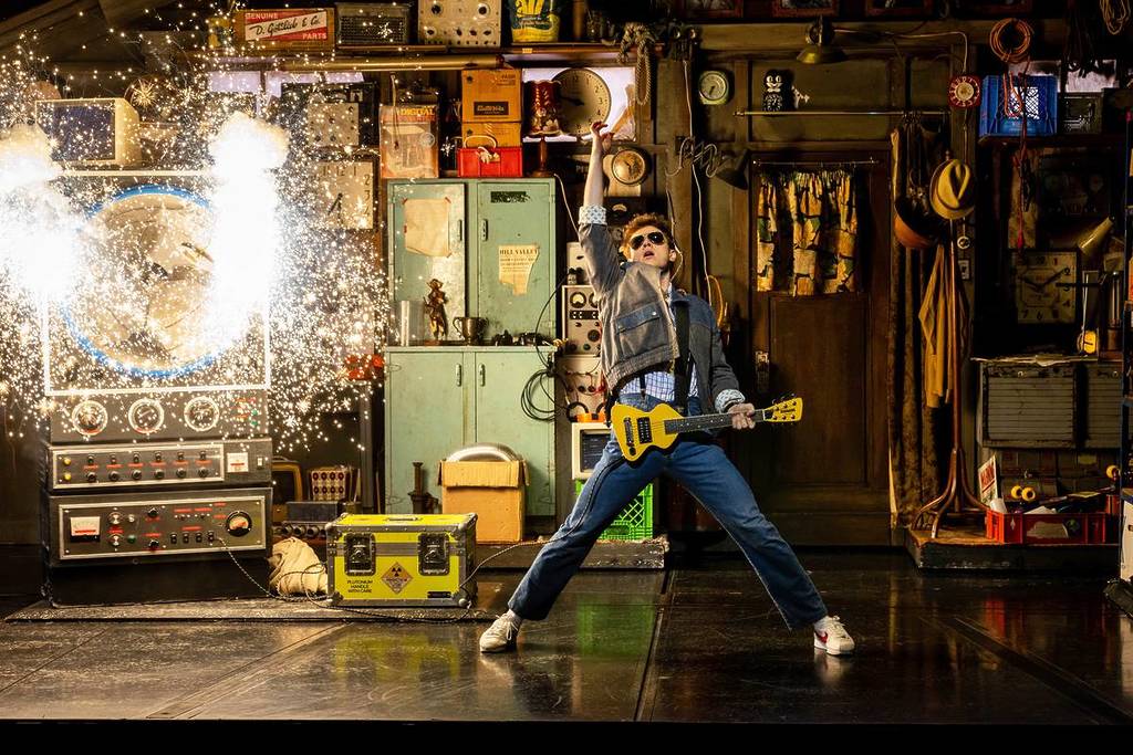 ben joyce as marty mcfly onstage in back to the future the musical after a strum of a guitar with sparks in the background