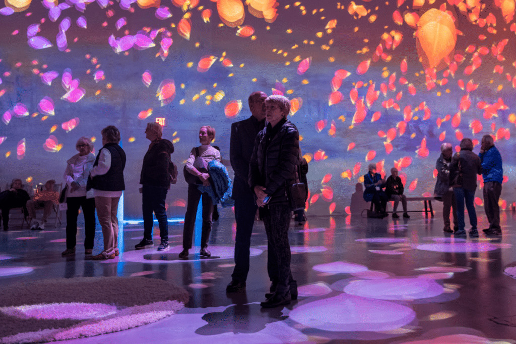 couple stands in a room as digital projections of petals tumble down