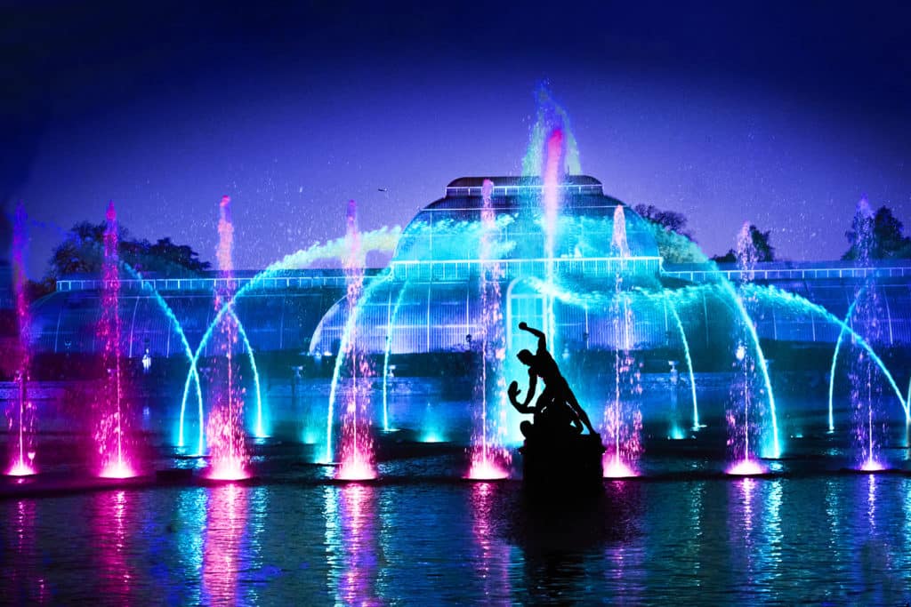 the palm house light show at kew's christmas trail, with purple and blue illuminated jets of water lighting up the scene