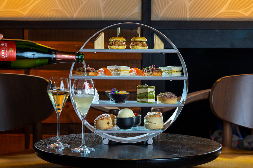 a four-level circular afternoon tea stand with sweet treats, and a bottle of champagne being poured into a glass in the foreground at The Prince Akatoki