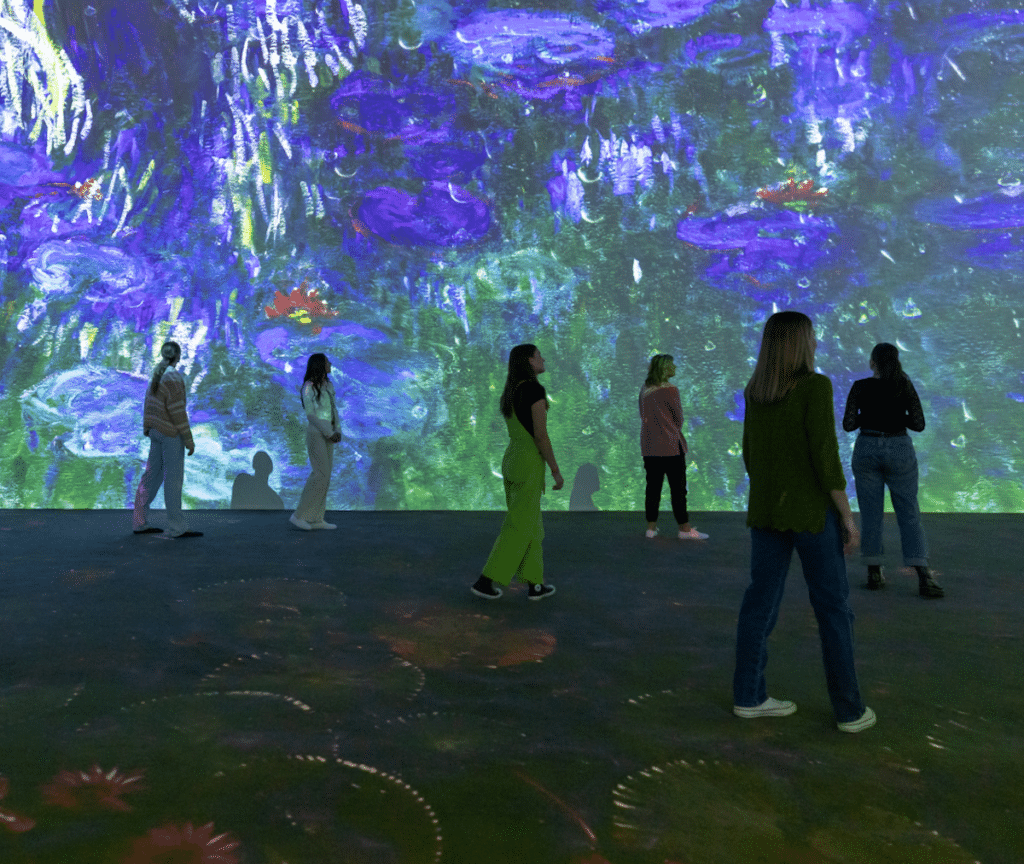 A group of people walk around among giant projections of Monet's waterlilies