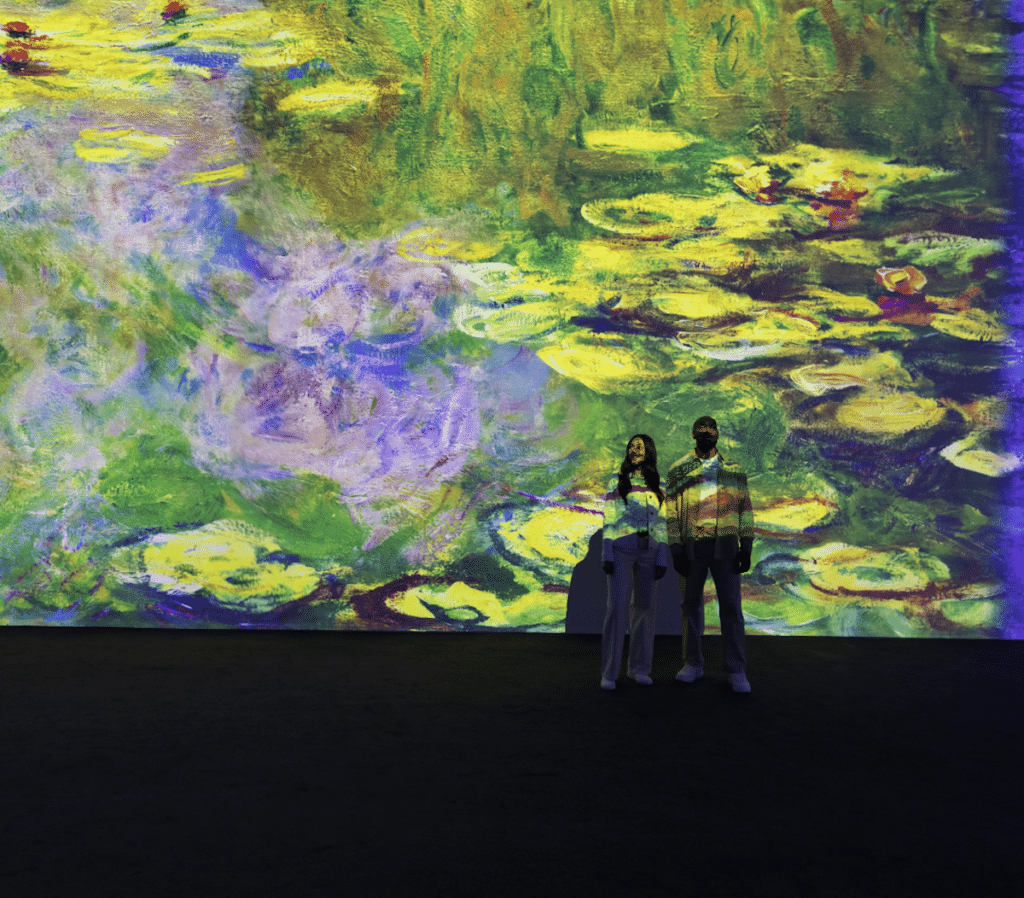 a couple stand against a wall bathed in a giant projection of Monet's water lilies